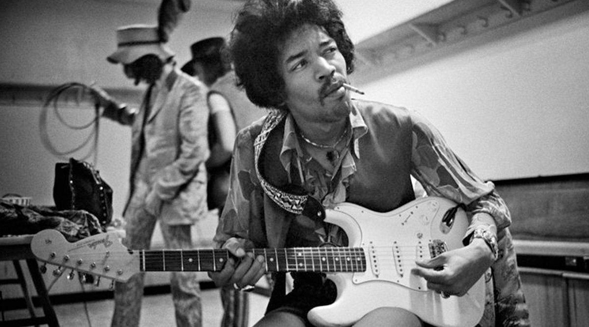 Jimi Hendrix chooses a new guitar. In the background, the sales assistant selects the wires of the desired length.